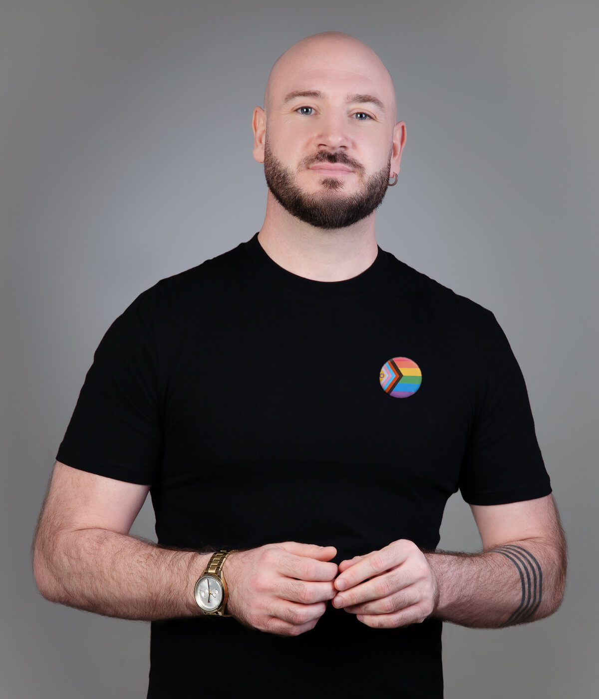 Martyn wearing a black t-shirt and rainbow flag pin in front of a grey backdrop.